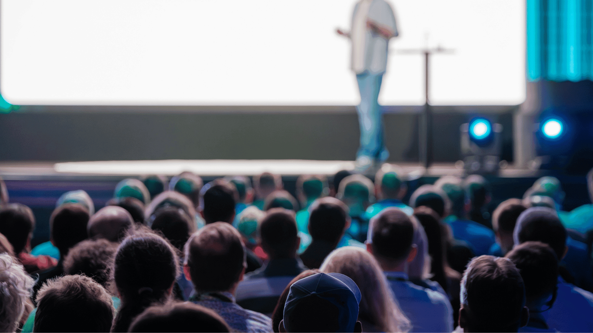 Audience members watching a speaker present on stage at a professional conference.
